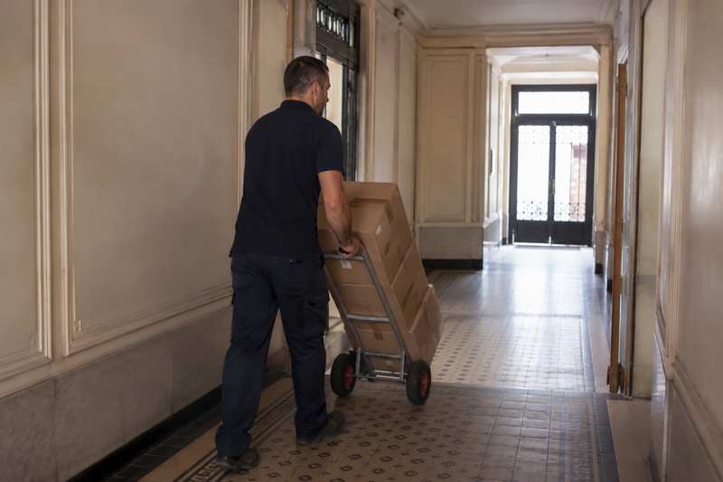 Débarrasseur poussant un diable chargé de cartons dans un couloir
