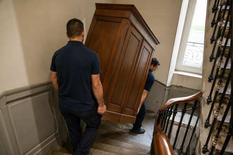 Deux débarrasseurs descendent une armoire par un escalier